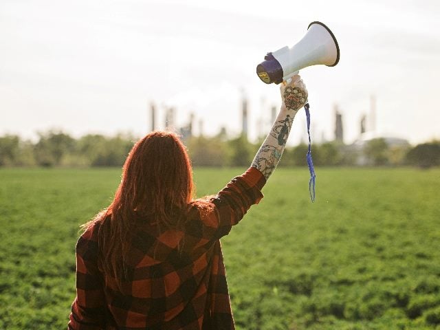Rear view of woman with megaphone outdoors.