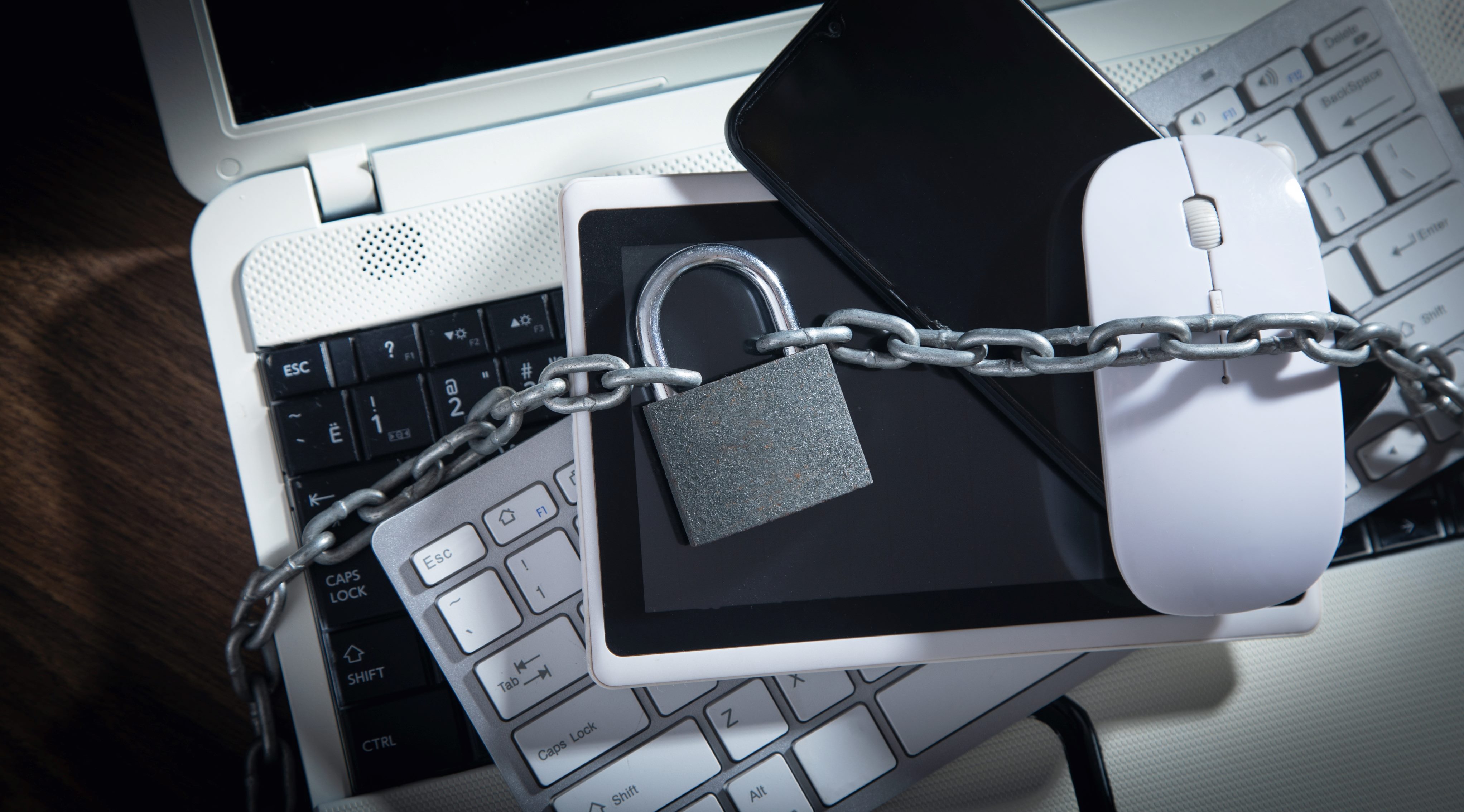 A laptop, keyboard, mouse, tablet and smart phone are surrounded by a chain and locked with a padlock in piece about strategic technology investments.