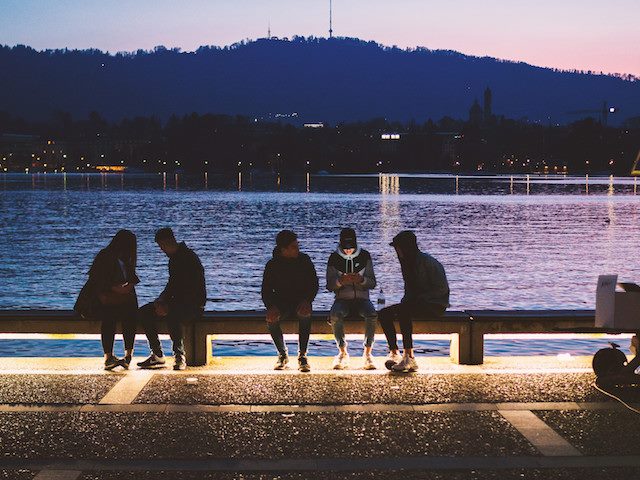 group of young people on bench outdoors, all looking at their phones
