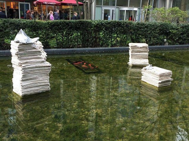 Newspaper stacks over water in a public art display.