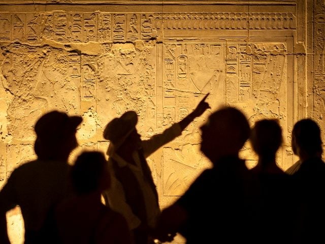 Group of unrecognizable tourist archeologists standing in silhouette in front of ancient Egyptian hieroglyphs, representing a CX leader guiding people to great VoC programs.
