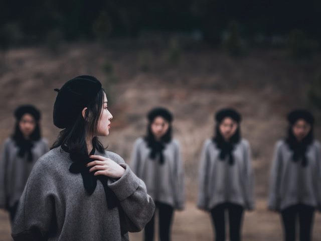 five women dressed in identical outfits. one stands in foreground, looking over her shoulder at the others