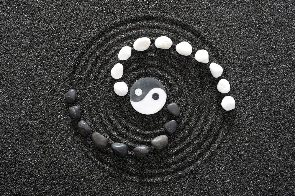 A zen design in black sand with the yin and yang symbol in the center with black and white stones flaring out on each side in a piece about aligning CX and EX in business.