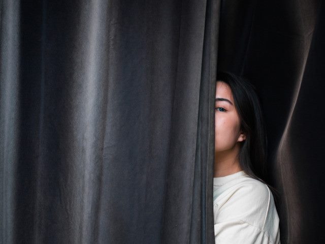 woman peeking out from behind a curtain