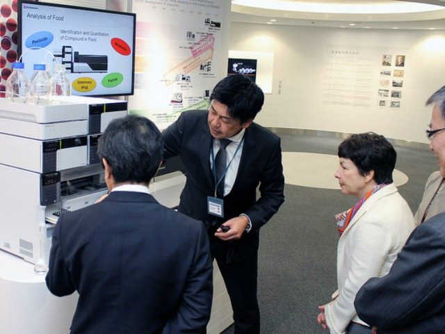 Two men demonstrate how a machine works to two people.
