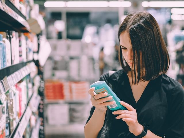A young woman with dark hair and wearing a dark blouse studies a personal product in a store before deciding whether to purchase it. 