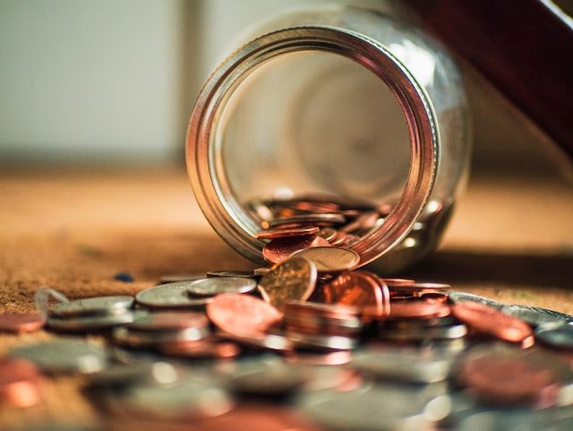 Coins spilling out of a toppled over glass jar 