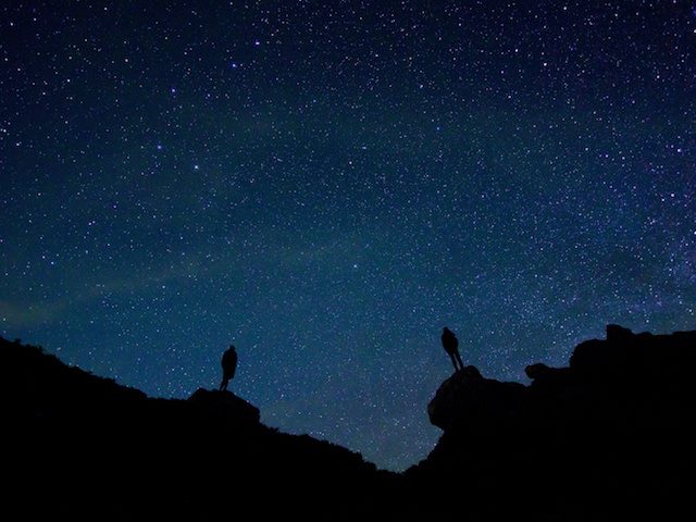 two people standing on separate rocks against a night sky