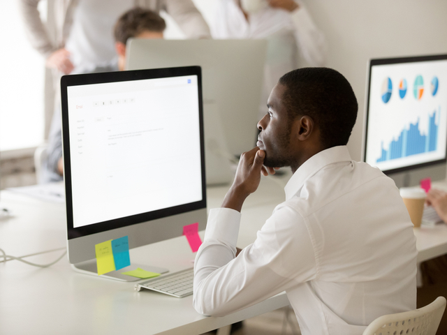 An employee thinking over a business email, while working on computer in office.