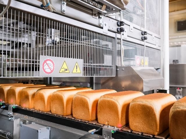 Loaves of golden baked bread on a conveyor belt being produced by automated machinery in a factory, suggesting the importance of customer experience automation in enhancing CX.