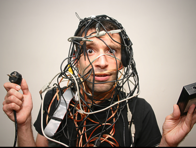 An office worker tangled up in a bunch of computer wires and power cords. - Digital Chaos Concept