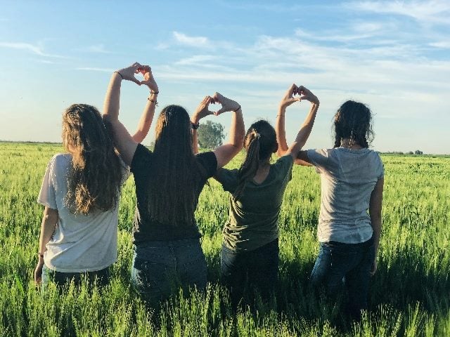 Four women holding hands, as they make heart signs.