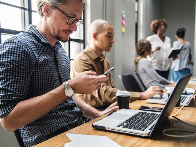 man looking at phone while sitting at workplace computer