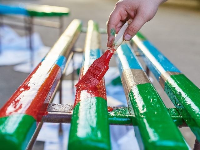  Brush in hand paints a red section on a bench filled with several colors. 