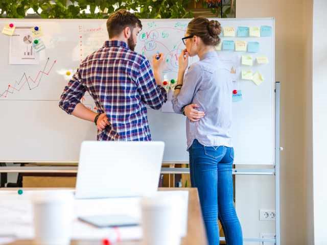 Two people building a strategy on the whiteboard.