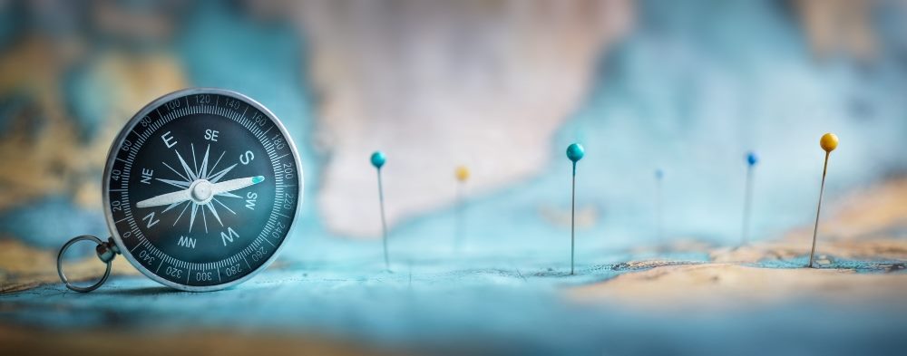 A map with a compass on the left and a series of straight pins with blue and yellow heads mapping out a journey.