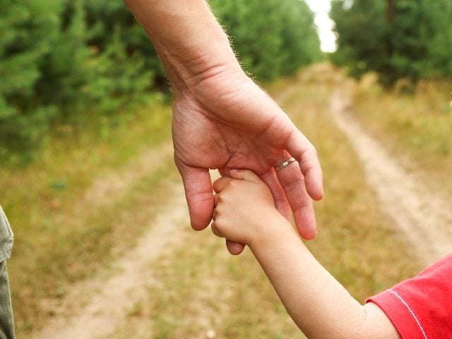 A father holds the hand of a small child as they walk down a country path that has wheel ruts and grass growing on it, indicating the importance of humanizing the brand-customer relationship. 