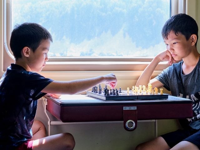 Two young boys dressed in dark T-shirts play chess while traveling on a train, suggesting the importance of AI and next best actions in decision making. 