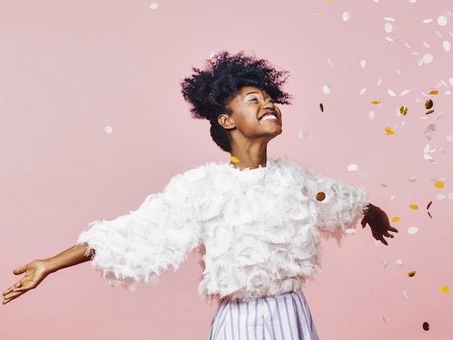 a young  woman looking  very happy, arms outstretched, confetti  falling around her