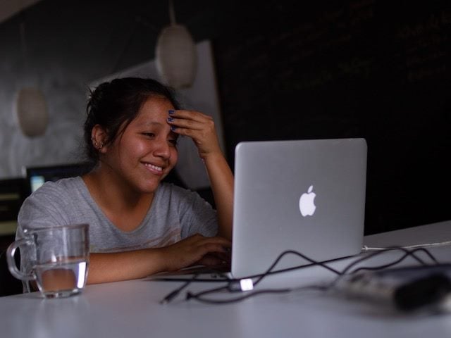 smiling woman looking at her laptop, leaning her head in her hand