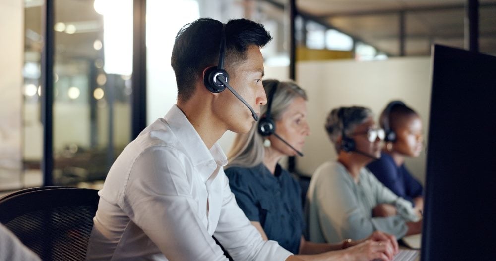 Agents working in a contact center and rendering customer support and service while using computers and wearing headsets in piece concerning contact center agent well-being.
