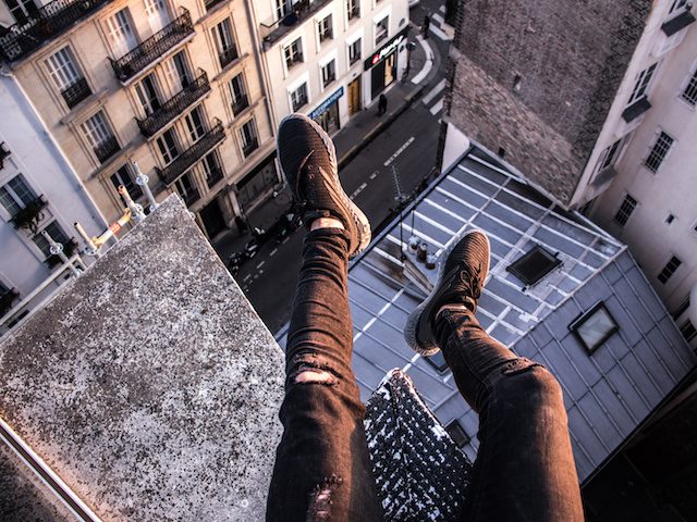 person sitting on top of a building with legs dangling over a high drop
