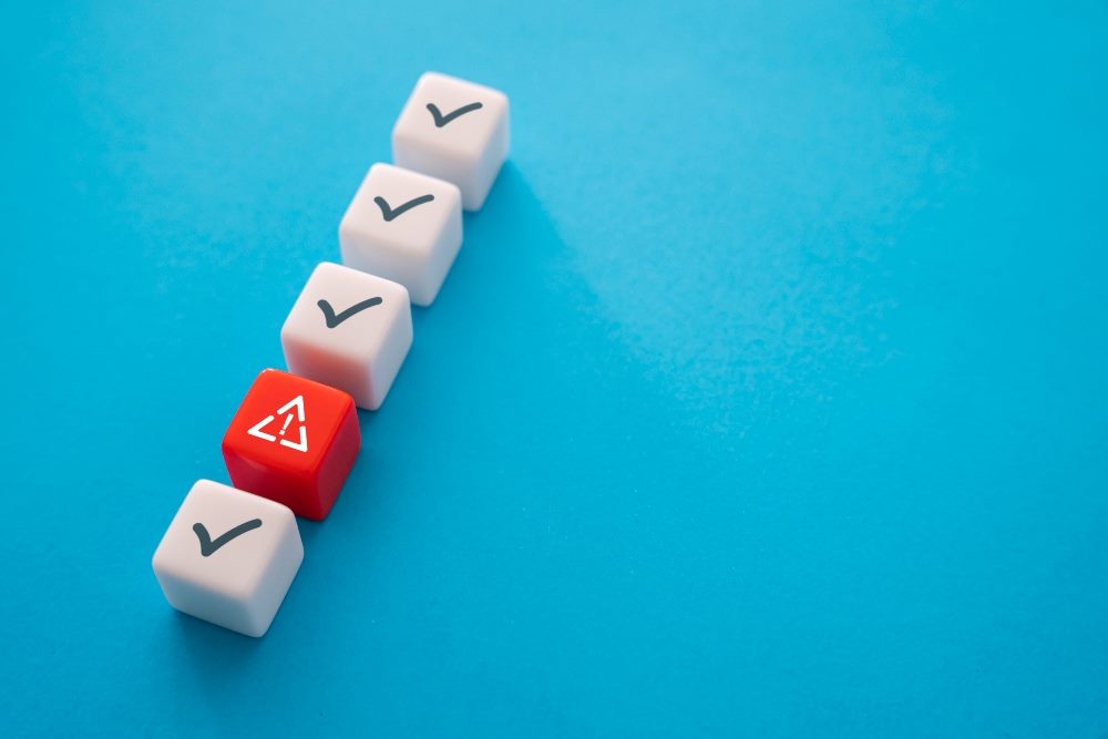 Five white cubes in a row with four of them white with black check marks and one red with an exclamation point inside a white triangle in piece about UX design strategies and errors.l
