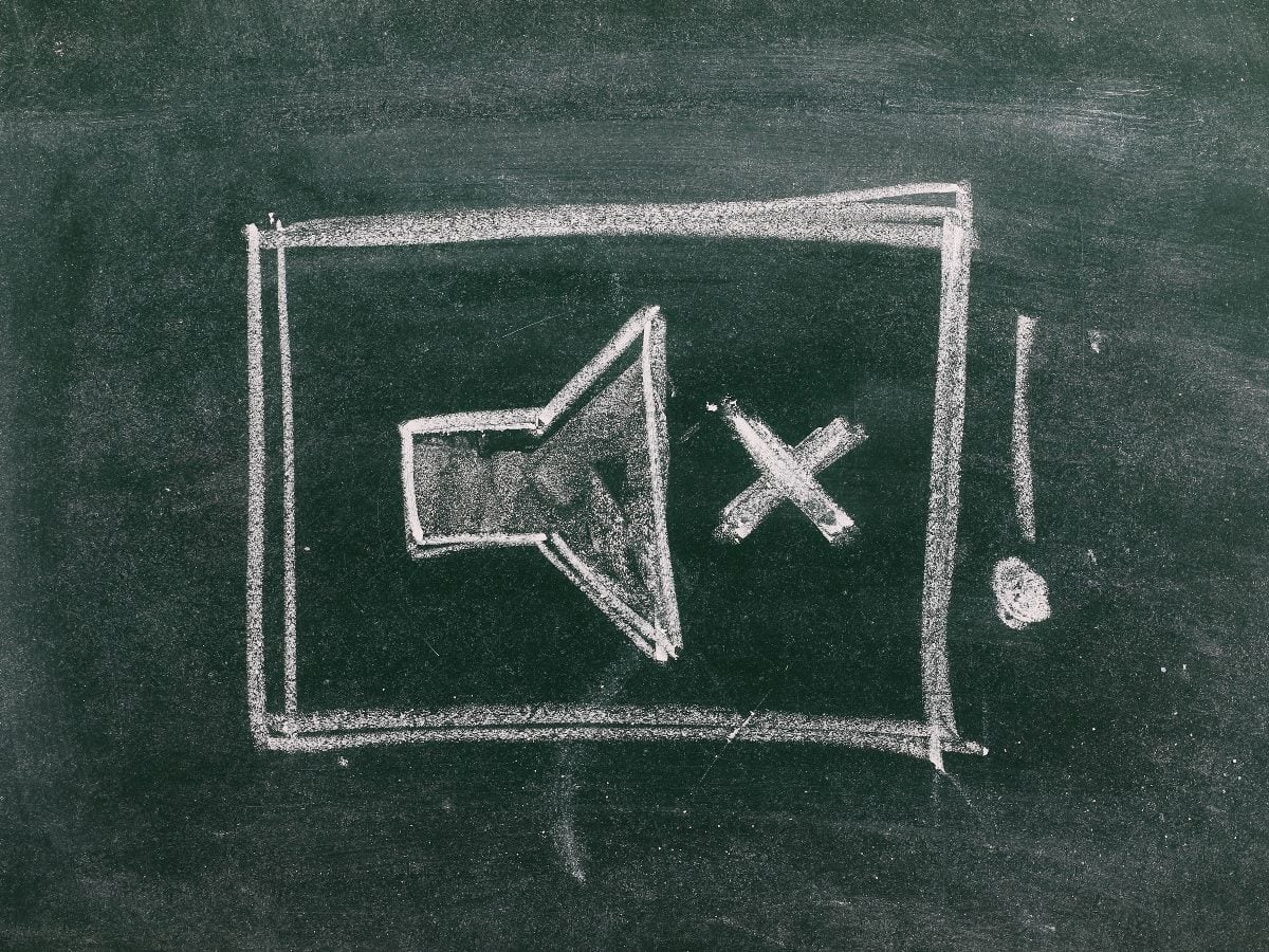 Chalk drawing of a muted speaker icon and exclamation mark on a blackboard, symbolizing silence, communication breakdown or muted alerts.