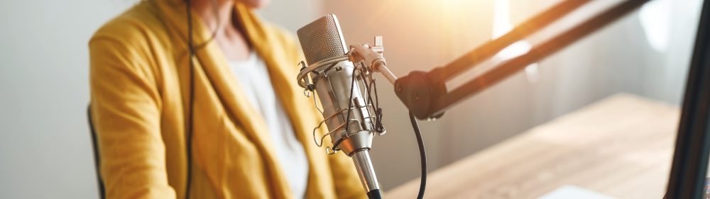 A shot of a podcaster 's chest and torso wearing a yellow jacket and white shirt in front of a microphone in story about YouTube's podcast discovery efforts.