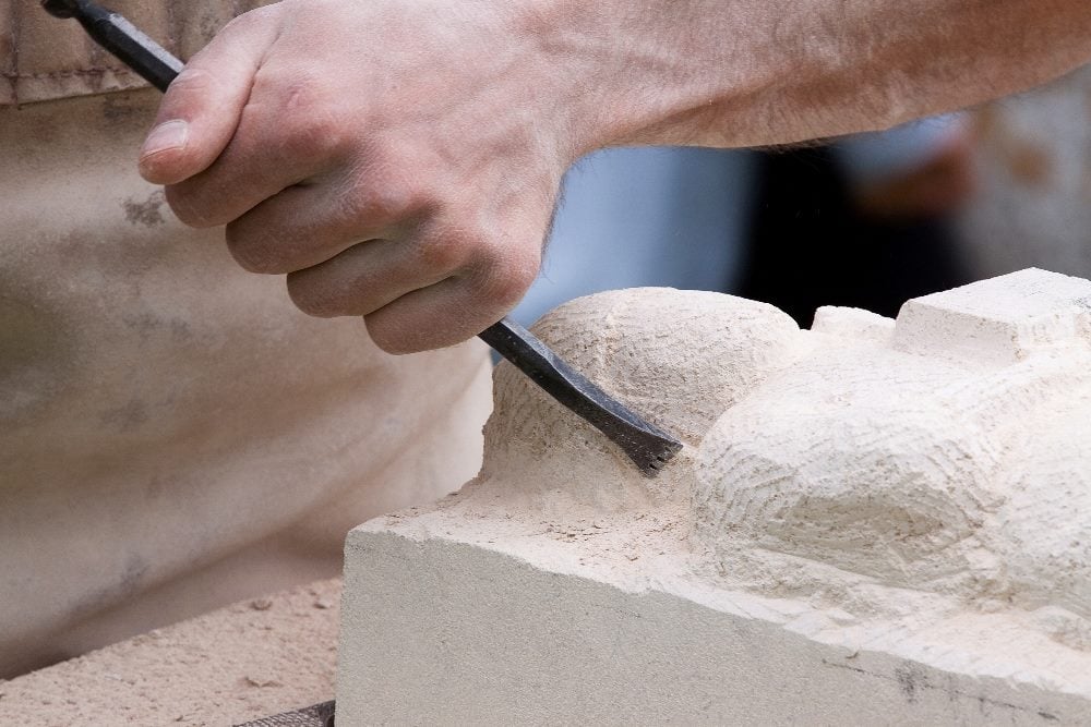 Close up of a sculptor holding a chisel and working on a piece of stone in article about B2B thought leadership.