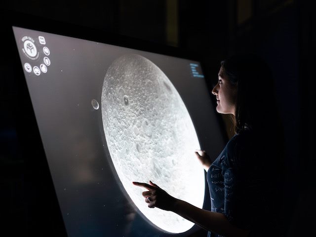 a woman looking at a rendering of the moon in detail on a screen