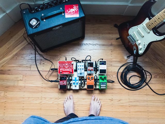 bare feet near a group of guitar pedals with cords plugged in