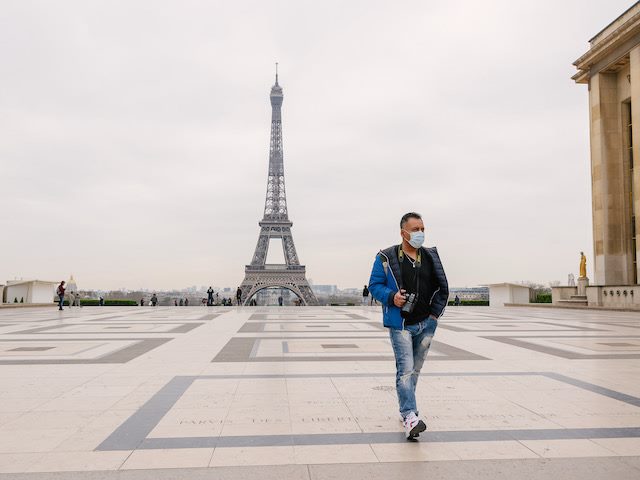 man walking in Paris,  in front  of the Eiffel Tower,  wearing  a mask