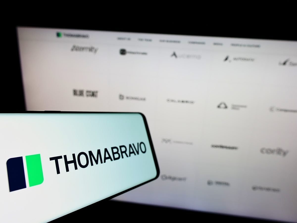 A smartphone displaying the Thoma Bravo logo in the foreground with a blurred background screen showing logos of software and technology companies associated with the private equity firm.