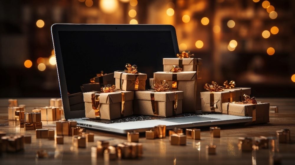 Tiny gift boxes wrapped in gold foil and bows sit piled on and around an open laptop in piece about customer engagement during the holidays.