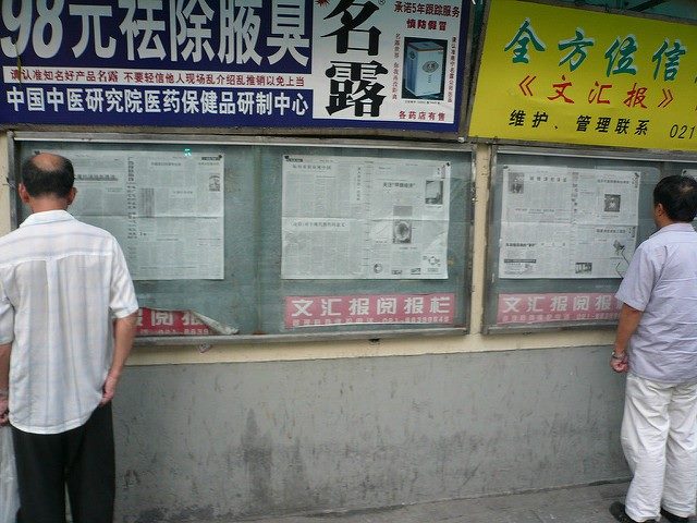 Two men staring at a newspaper wall.