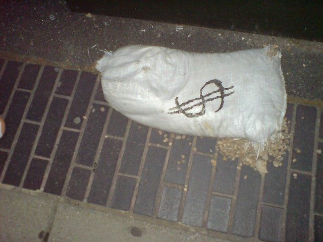 A white bag with a dollar sign stuffed with an unknown material laying on the ground.