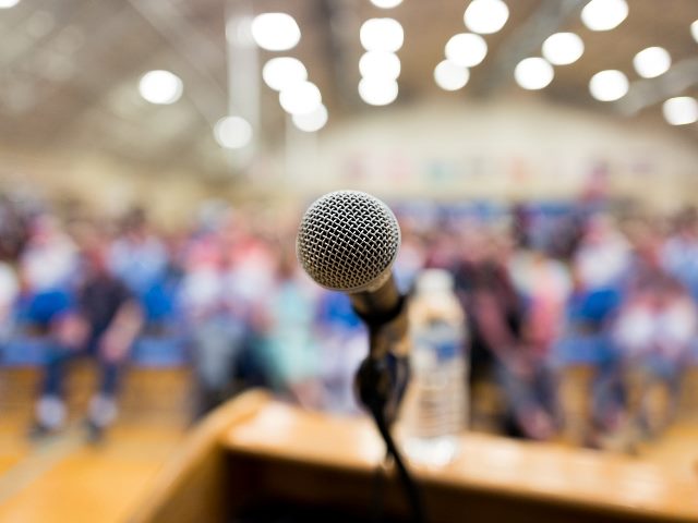 Microphone on podium with blurred audience in background, representing someone giving a state of digital customer experience speech.