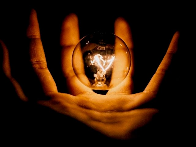 close up of a hand holding a lit lightbulb