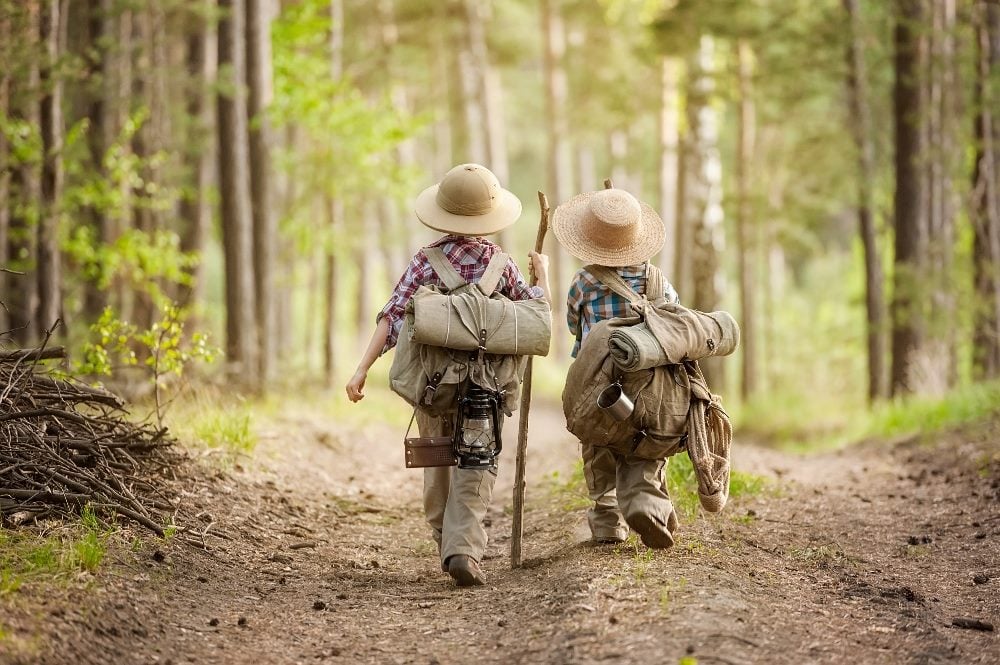 Two children walk through the forest wearing adventure clothing and carrying large backpacks in piece about retail trends.