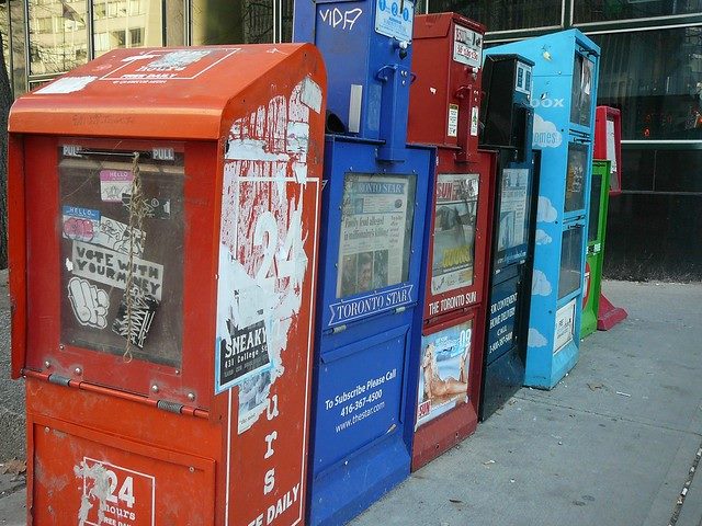 Row of newspaper boxes on a street.