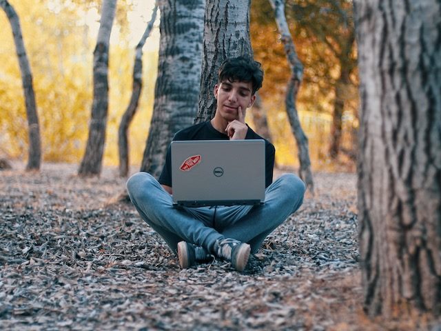 working outside on a laptop in the middle of many trees 