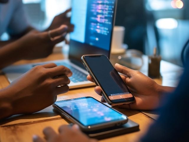 Programmer test coding technologies with mobile phone for comparing mobile and desktop website for user experience in piece about user experience analysis. 