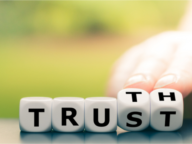 Hand turns dice and changes the word "Trust" to "Truth".