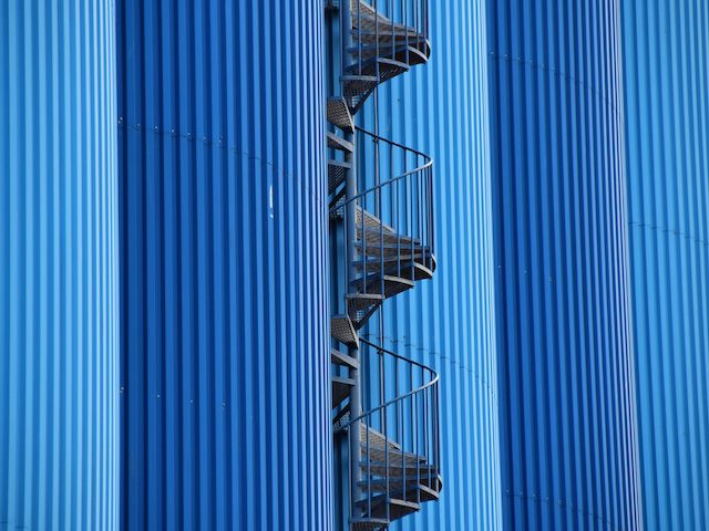 a series of five blue silos, side by side, with a spiral staircase in the middle