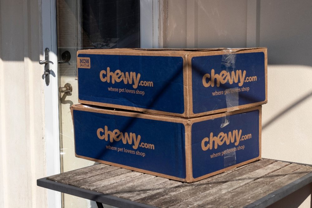 Chewy.com parcel boxes sit on a table outside a residence; Chewy is an online retailer of pet food and other pet-related products in a piece about frontline workers and customer empathy.