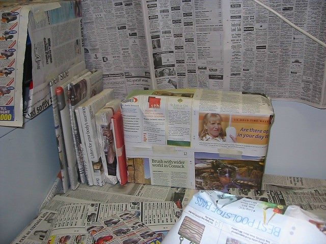 books bundled up in newspapers, and a wall with newspapers taped to it.