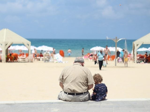 Picture from behind an old man and young child sitting down at a beach.