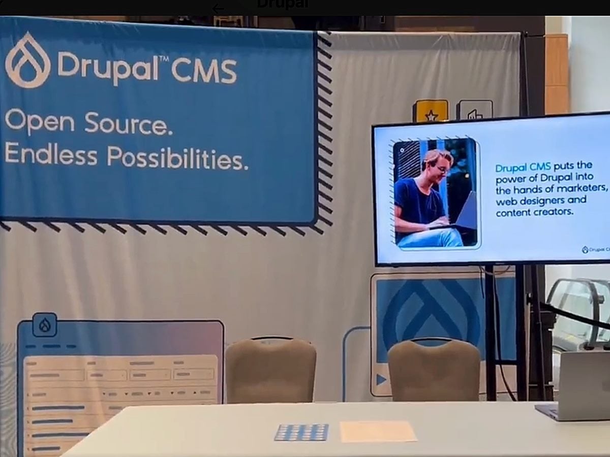 Drupal CMS trade show booth with large banner reading “Open Source. Endless Possibilities.” alongside a display screen highlighting Drupal CMS for marketers, designers and content creators.