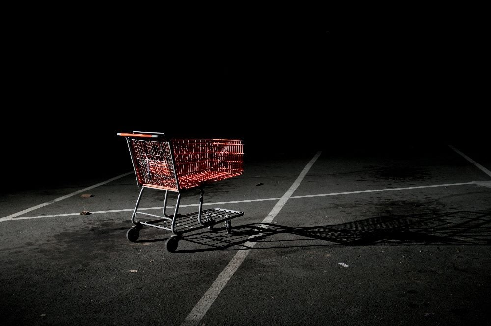 A lonely looking abandoned red shopping cart in a dark parking lot in a piece about customer experience trends.